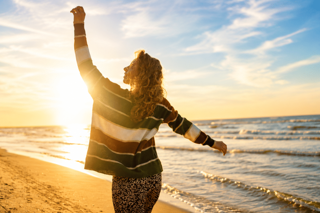 image of a girl walking along the beach, hands up, depictng emotions of happiness
