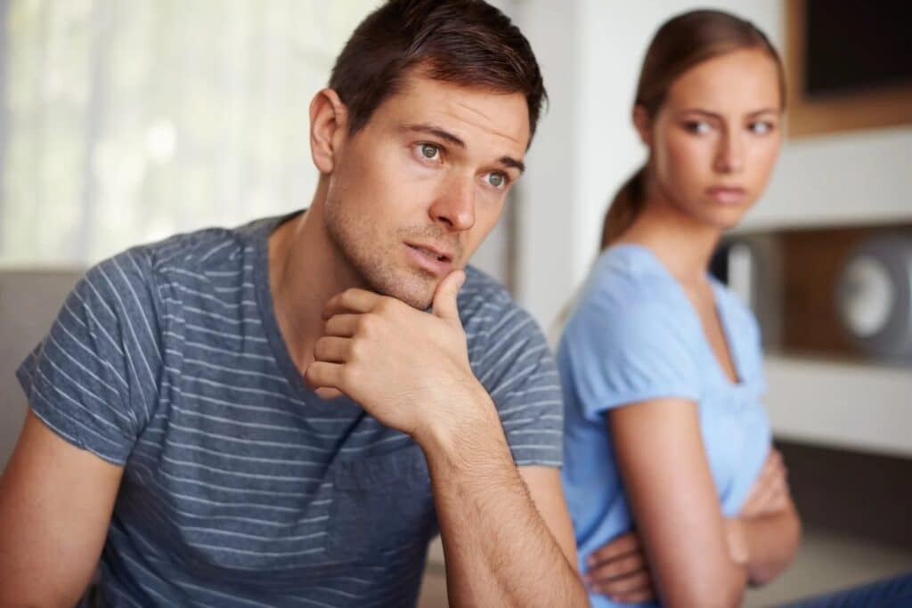 man looking distracted while wife is looking angry in the background