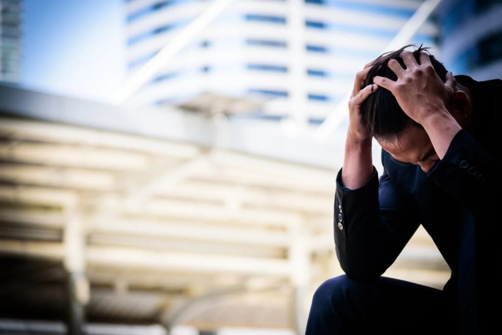 man looking stressed, head down, while outdoors