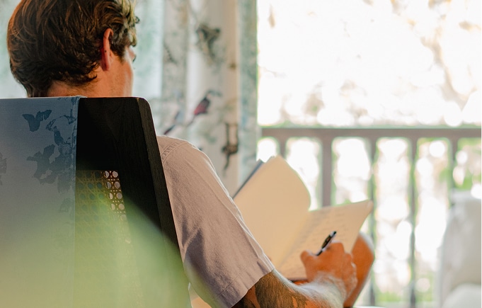 Person seated indoors writing in a notebook during a quiet reflective moment
