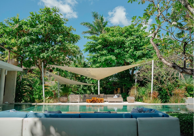 Outdoor swimming pool and shaded lounge area surrounded by tropical gardens at The Place Retreats in Bali
