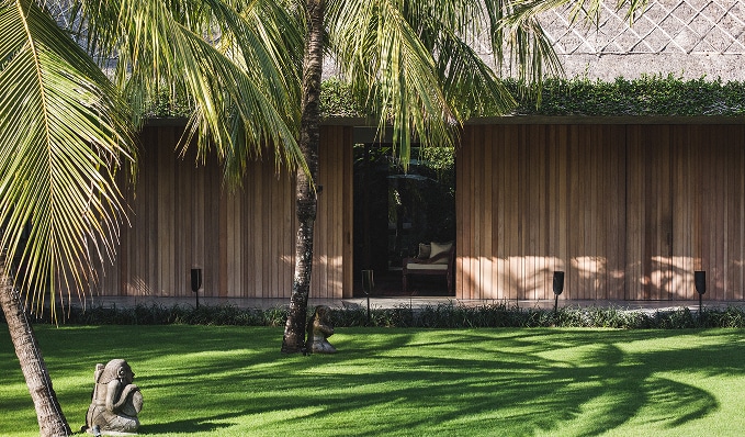 Palm trees and manicured lawn outside a wooden guest suite at The Place Retreats in Bali