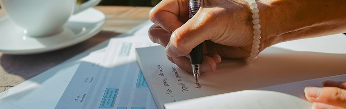 Close-up of a person writing notes on paper beside printed documents