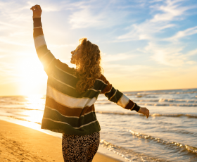 image of a girl walking along the beach, hands up, depictng emotions of happiness